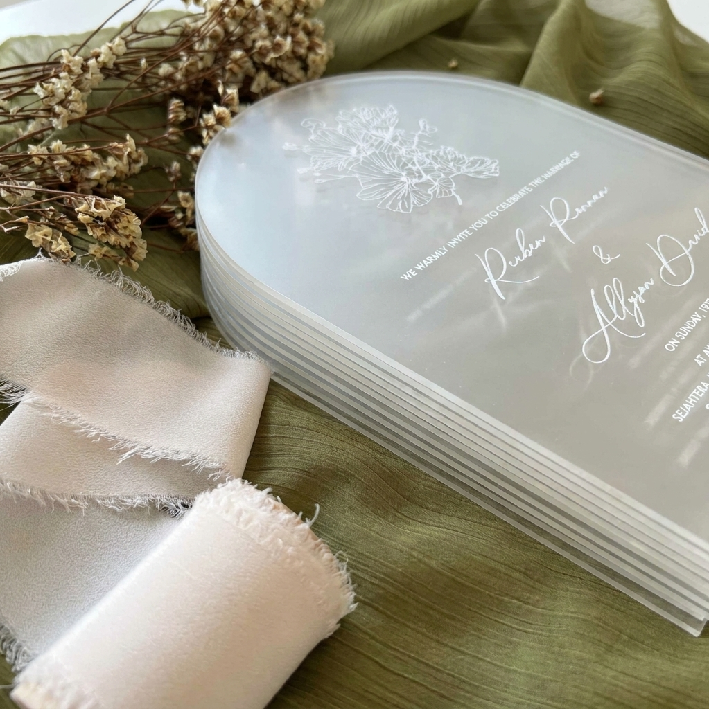Stack of personalized cards with floral design and text on a green surface with ribbons and dried flowers.