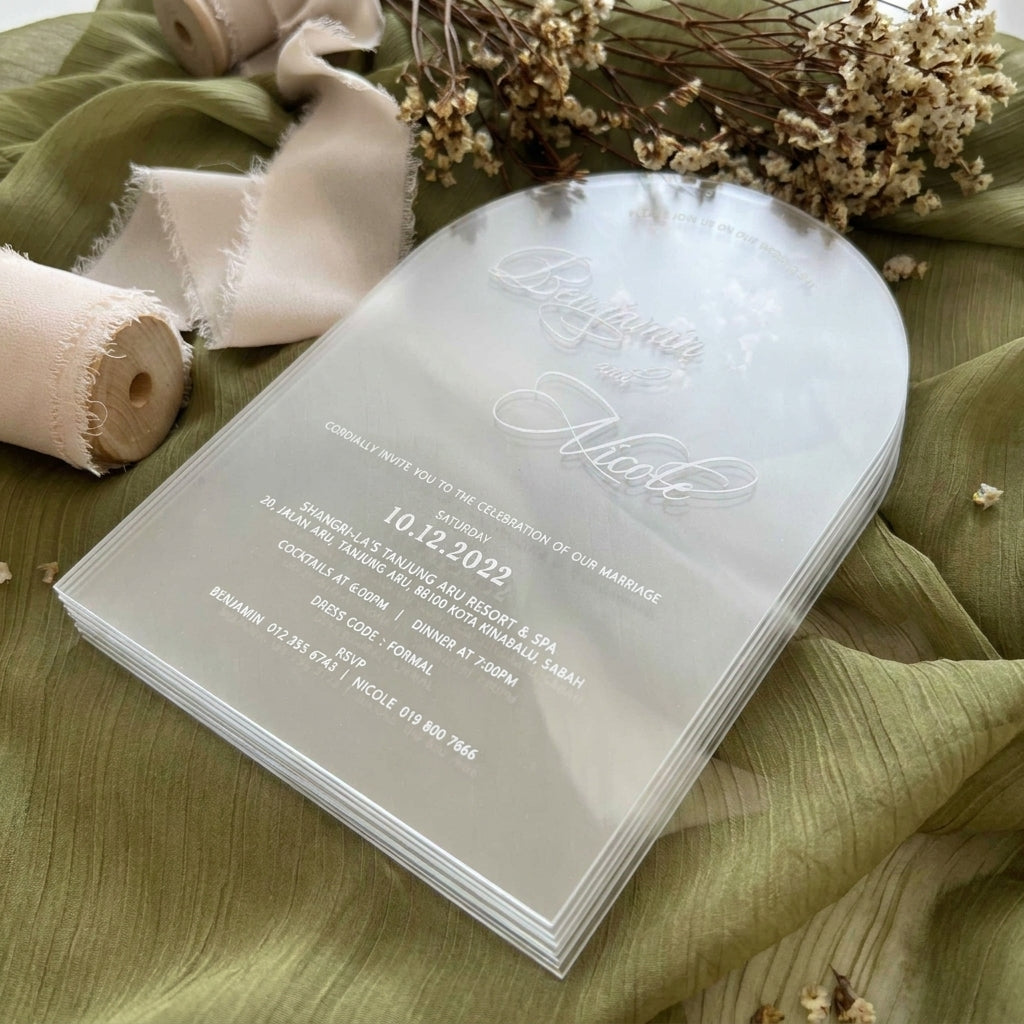 Stack of wedding invitations on a green fabric background with ribbons and dried flowers.