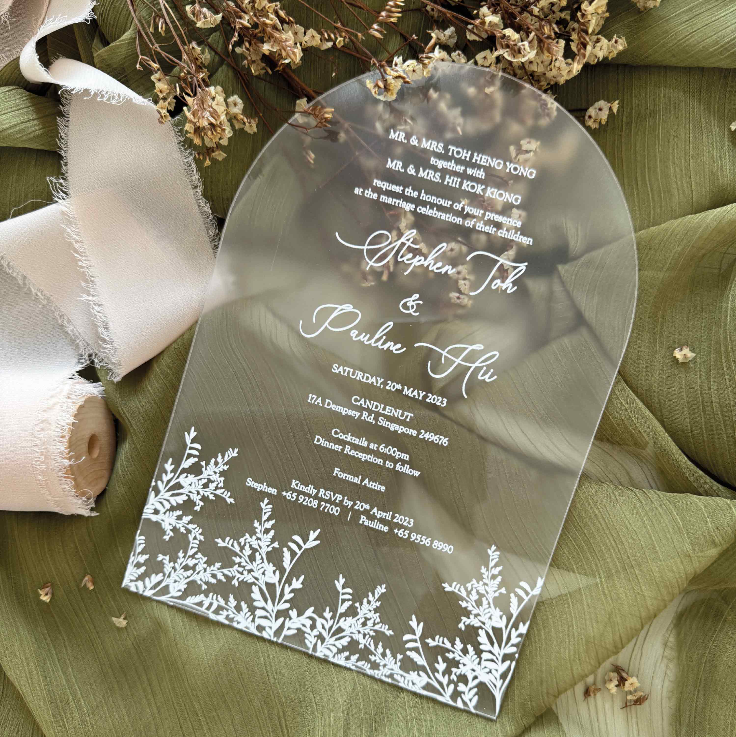 Clear wedding invitation with white text and floral designs on a green leaf background