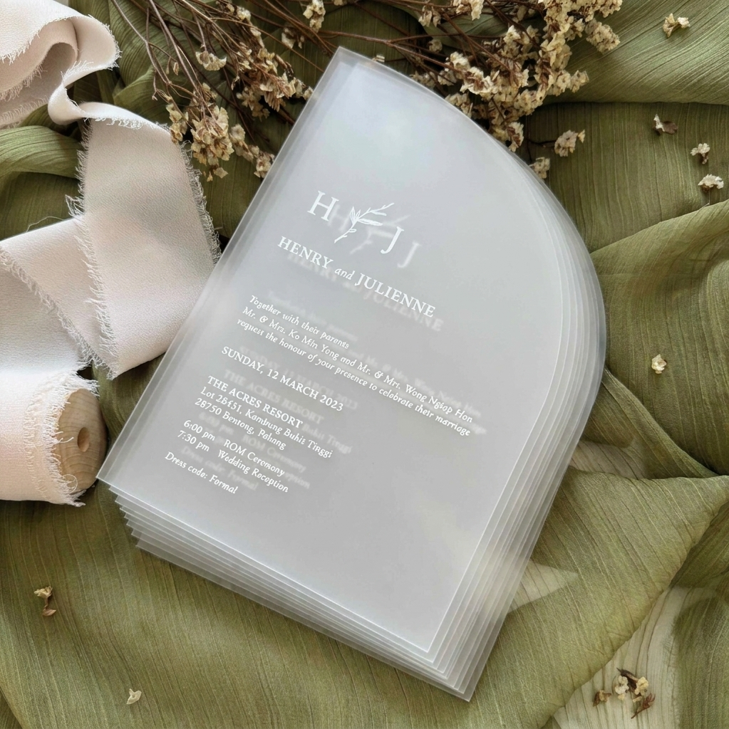 Stack of wedding invitations on a green leafy background with ribbons and flowers.