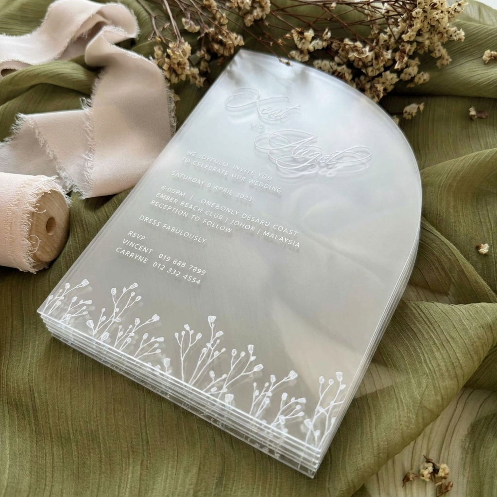Clear wedding invitation with floral design on a green fabric background