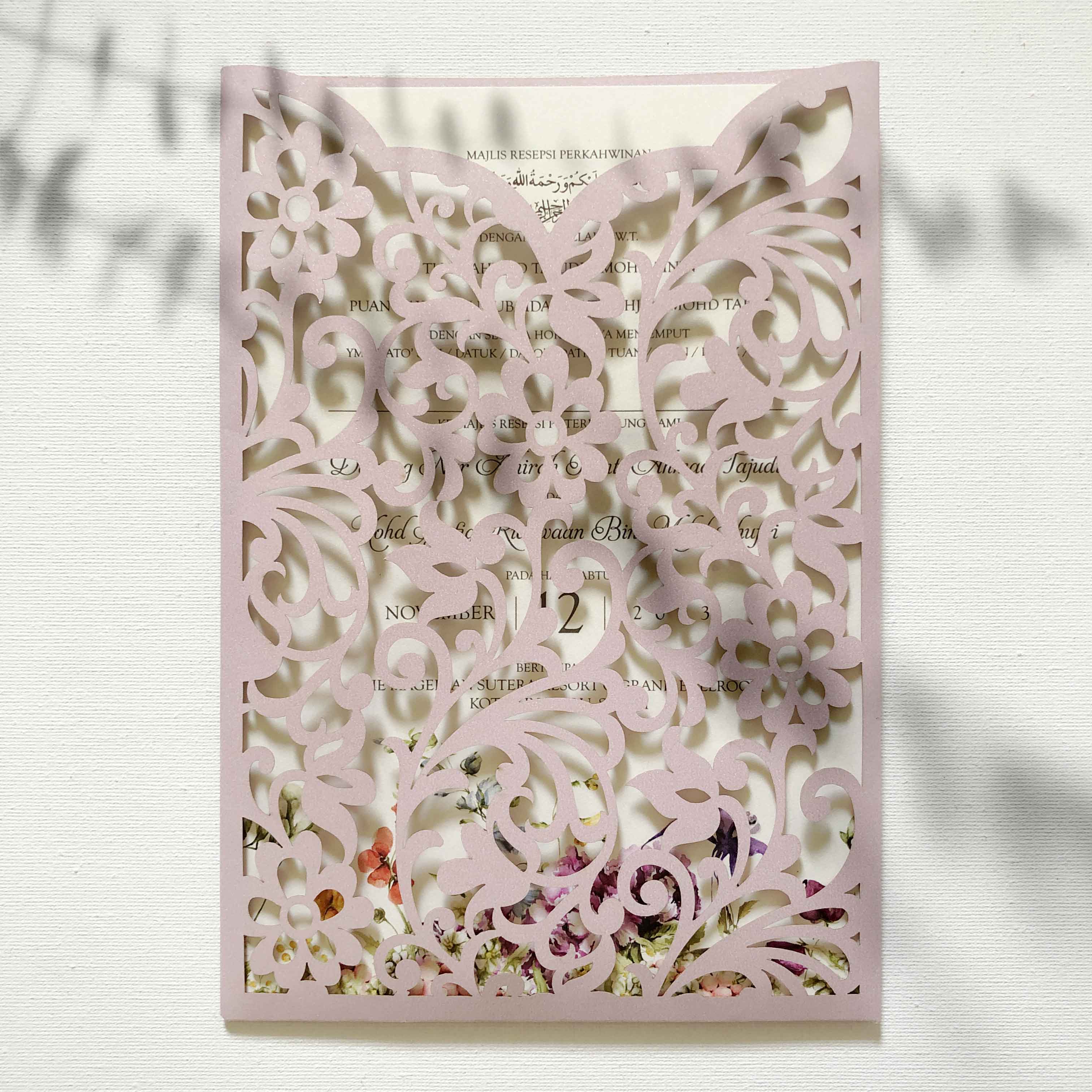 Decorative pink laser-cut invitation with floral elements on a white background