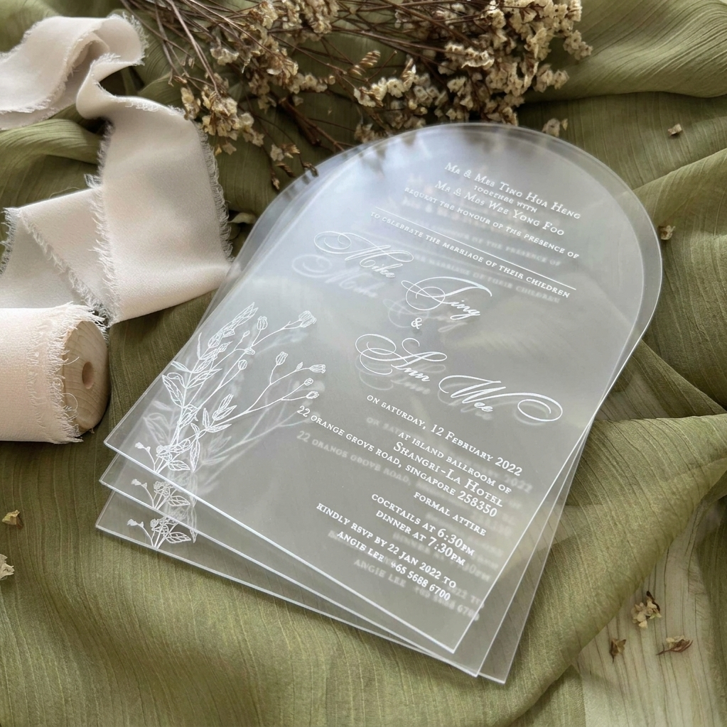 Clear wedding invitation with floral design on a green fabric background
