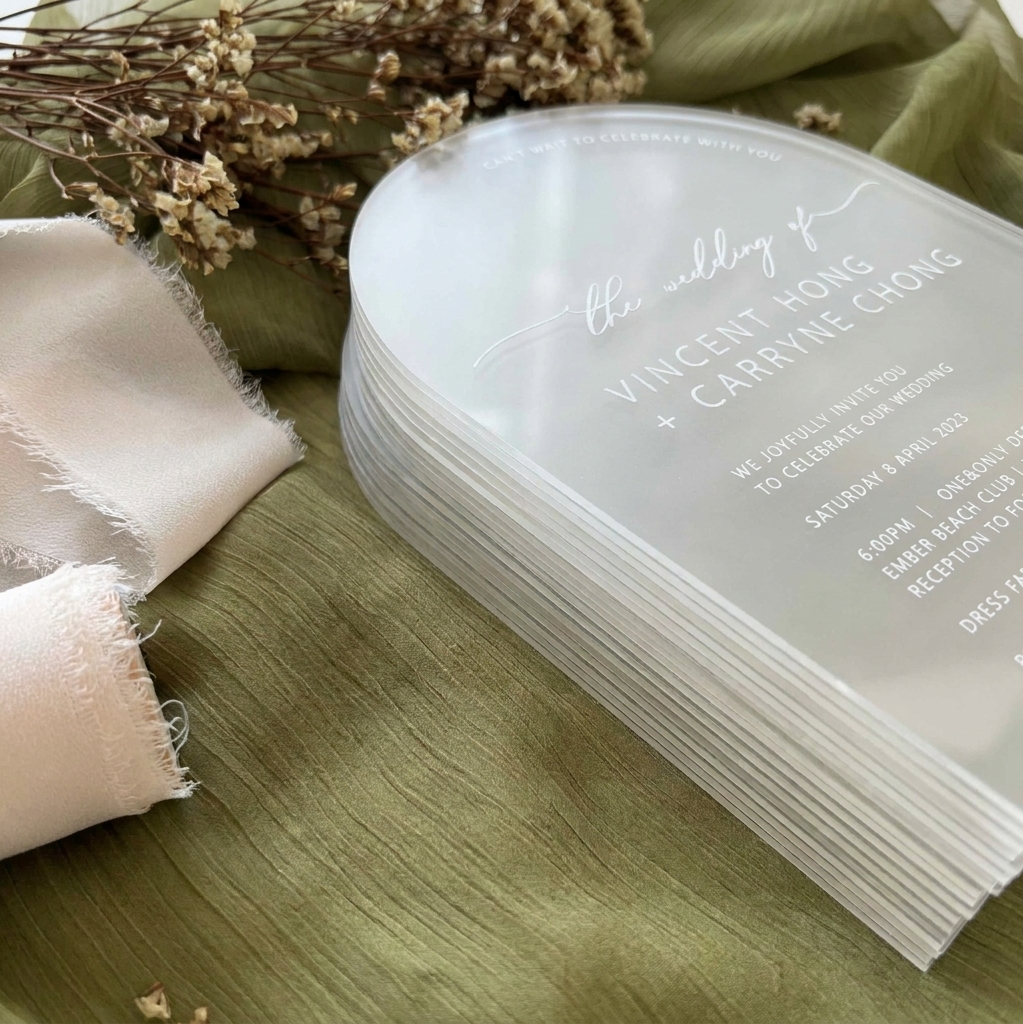 Stack of wedding invitations on a wooden surface with fabric and dried flowers.