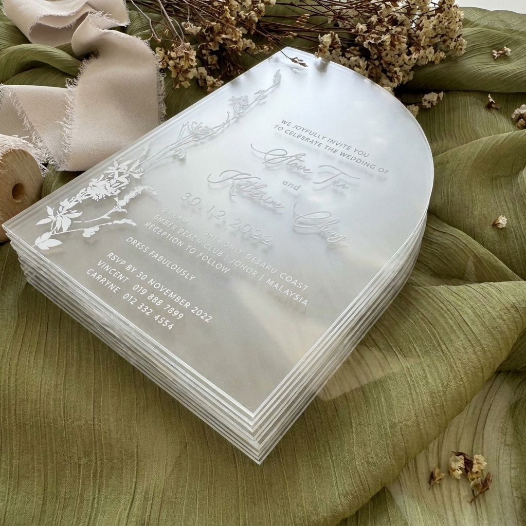 Stack of transparent wedding invitations with floral designs on a green fabric background