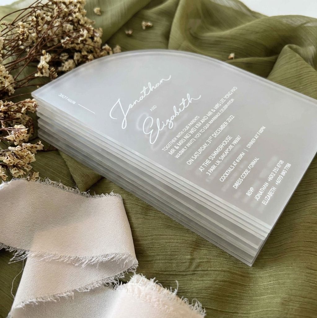 Stack of wedding invitations on a green fabric background with dried flowers and ribbon.